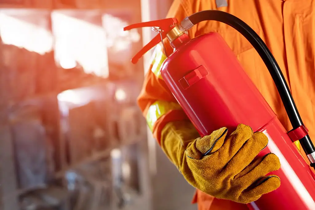Profissional de uniforme laranja segurando um extintor de incêndio